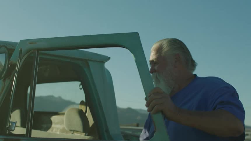 An elderly man exits an old pickup truck