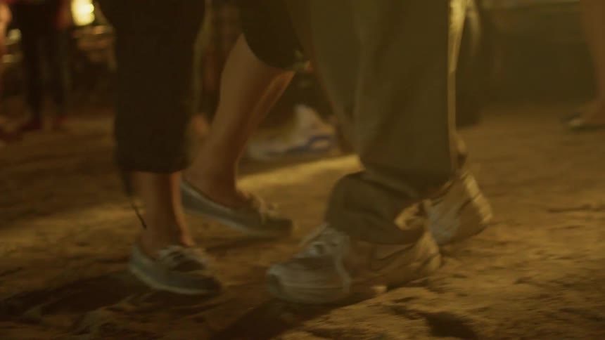 People are dancing together near their vehicles outside