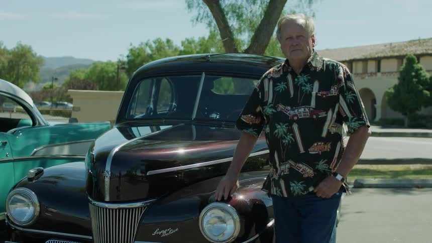 Man standing outside next to antique car on windy day