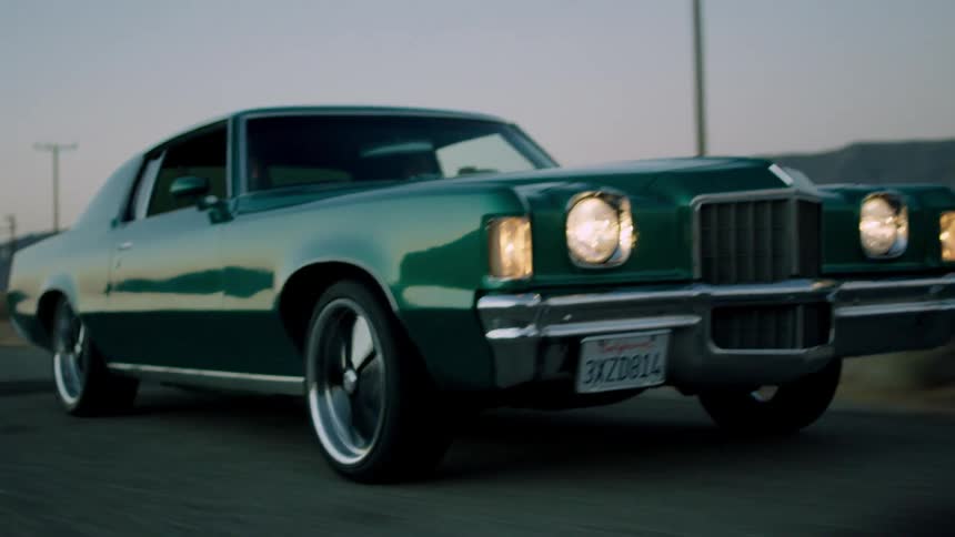A green car with spinning rims is driving down the street
