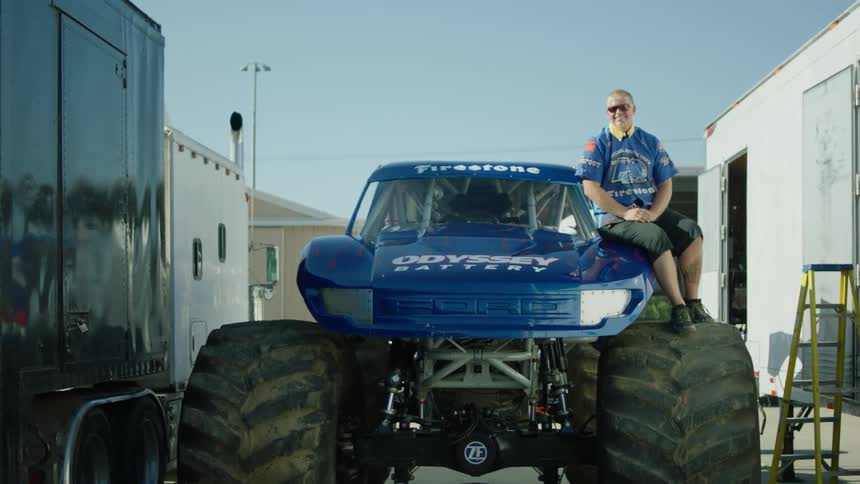 A man sits on the hood of a monster truck