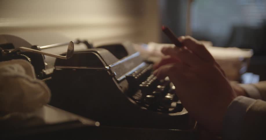 Someone smoking a cigar while sitting at a desk typing on a manual typewriter