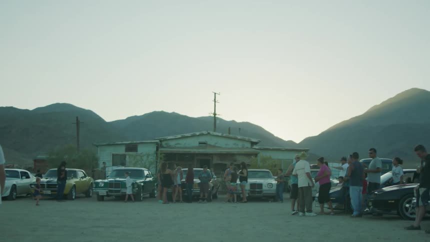A group of people gather together with old sports cars