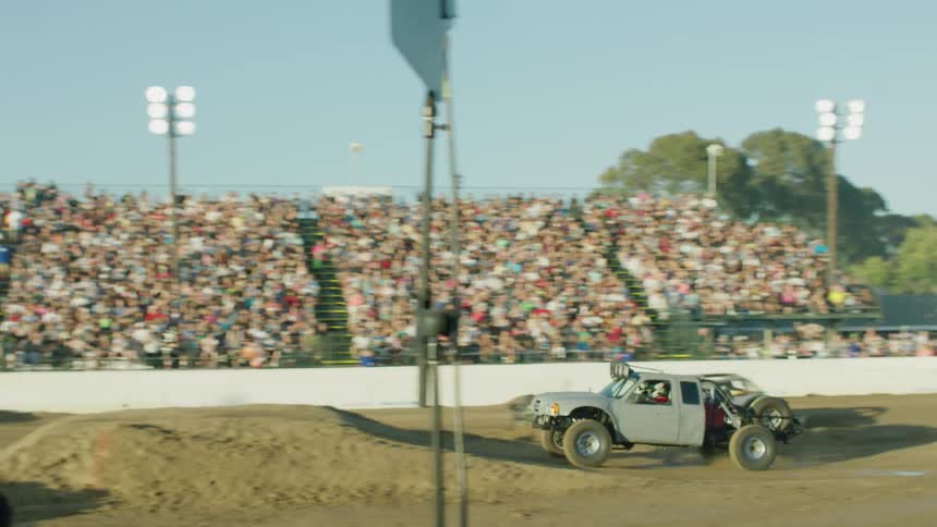 A truck performs a dirt jump as an audience watches