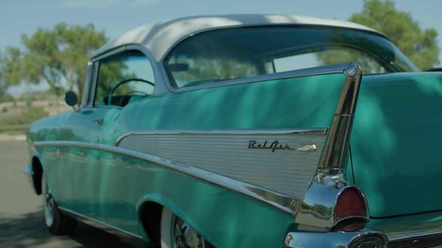An old teal green hot rod sits parked outside