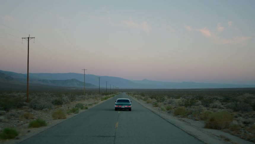 An old sports car travels down a desert road