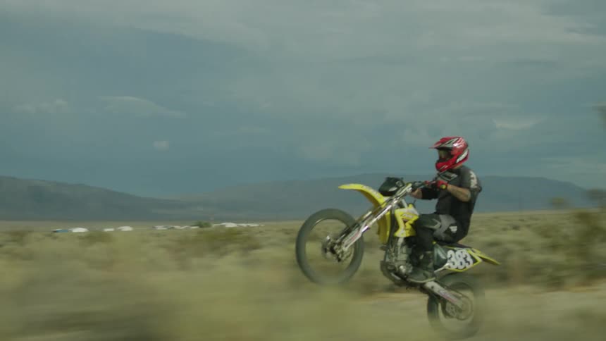 A man is riding his motorcycle off-road in a desert on a stormy day
