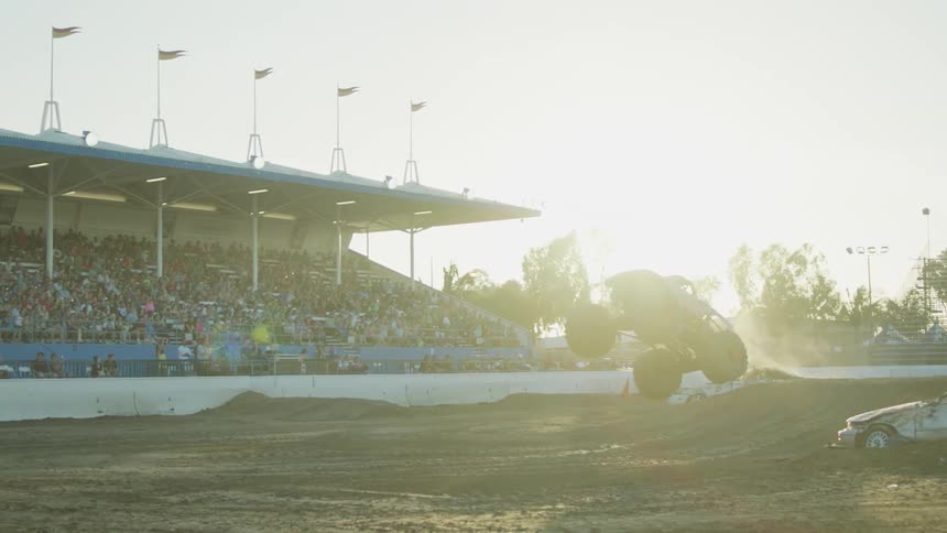 Monster trucks are jumping over cars at a fairgrounds