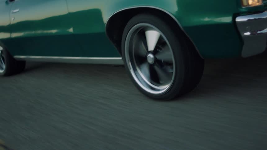 A green car with spinning rims is filmed close up as it drives down the street