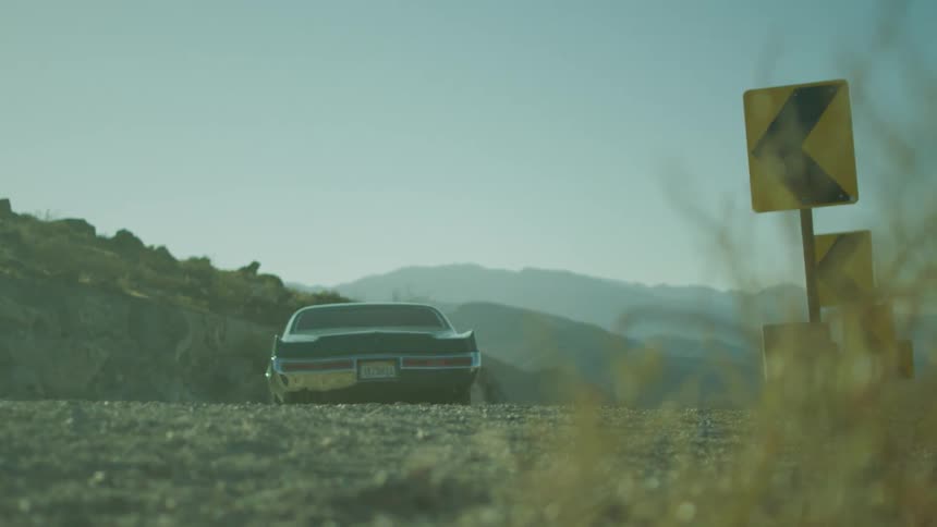 A green hot rod drives off on a gravel road