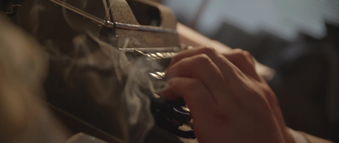 A man typing on a typewriter as a cigarette burns nearby