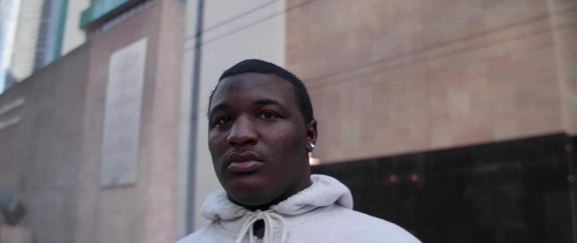 A man in a white hoodie stands in front of a building