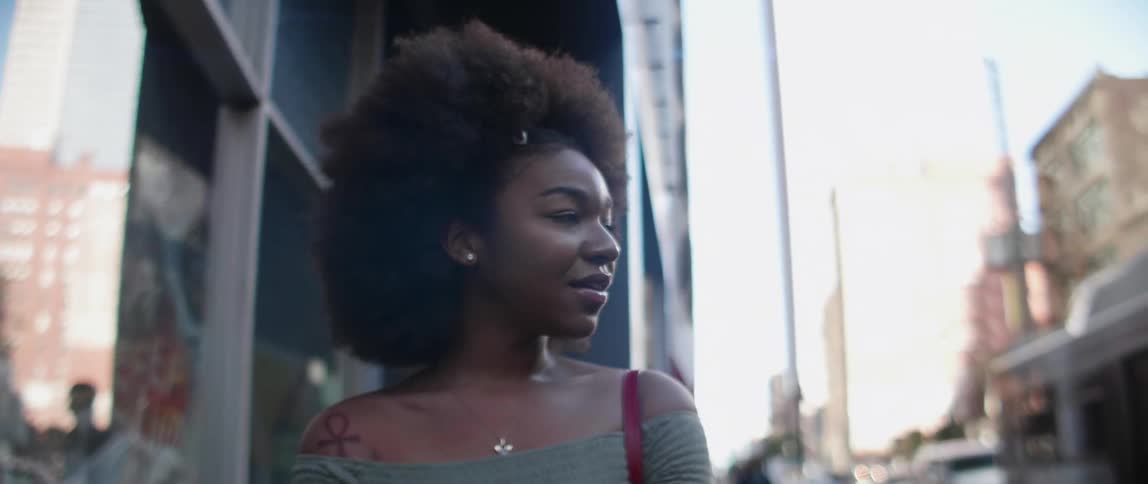A black woman stands outside of a city building and smiles