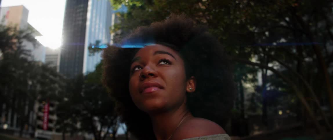 A black woman smiles and looks upward outside in the city