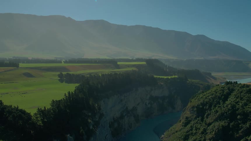 A lush green valley is split in the middle by a large gorge with a little river running through it