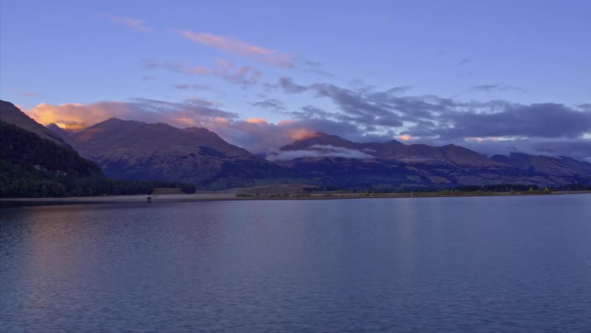 A drone flies over very calm water that looks at a mountain in the background