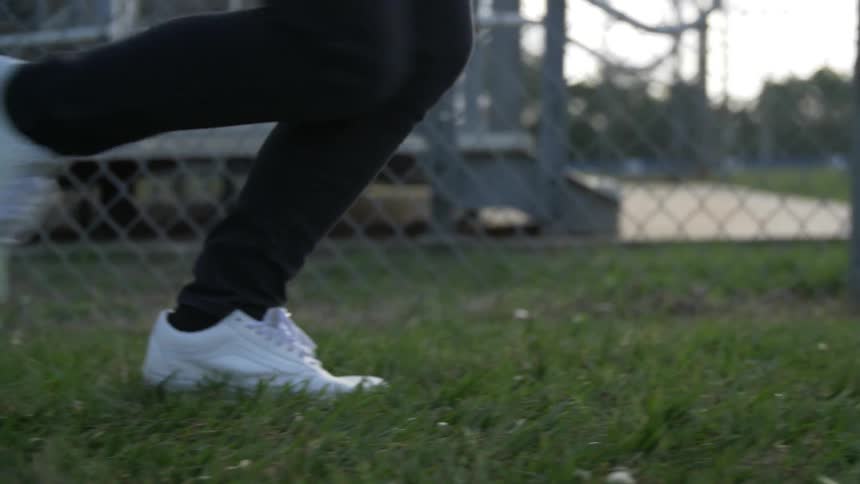 Two people run across the grass near a chain link fence