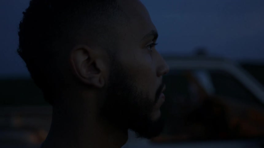 A black man stands outside of a pickup truck at night