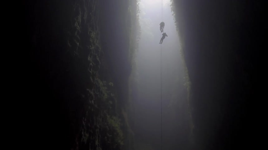 Two people cave dive into a cavern attached to ropes