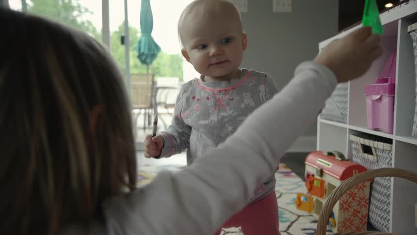 A baby and a young child are playing with a doll house together