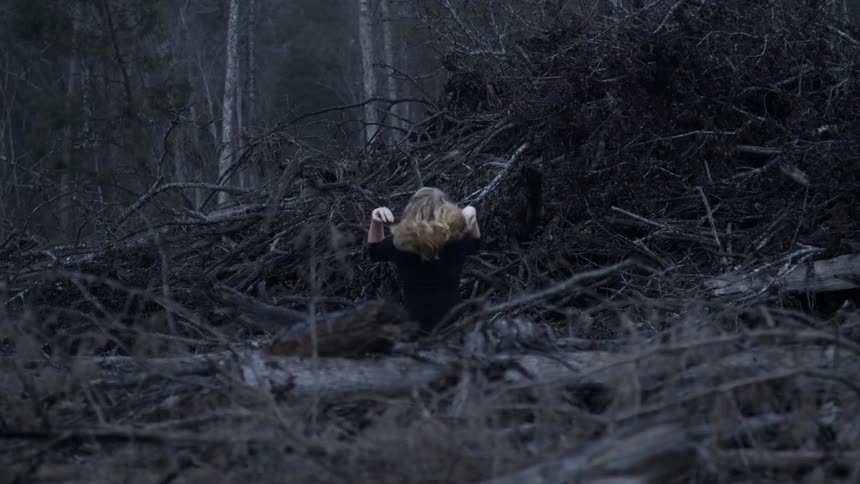 A woman sitting in the woods with her head between her knees
