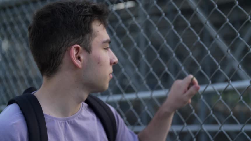 A man wearing a backpack looks through a chain link fence
