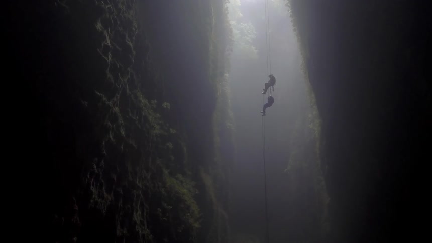 Two people climbing down a rope in a tall canyon