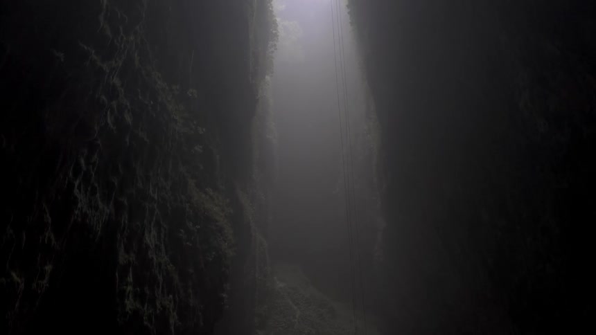A dark foggy cave with ropes on the side of it is filmed