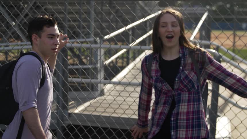 A boy is talking to a girl next to a fence and they both take off running together