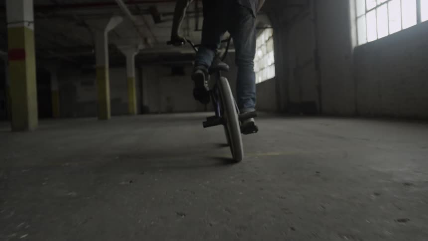 A man is riding a bike in an empty warehouse