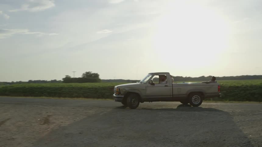 A pickup truck carrying workers backs up and heads off at dusk