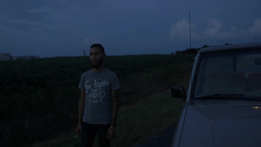A man holds a cigarette as he stand beside a pickup truck parked in the middle of a country road