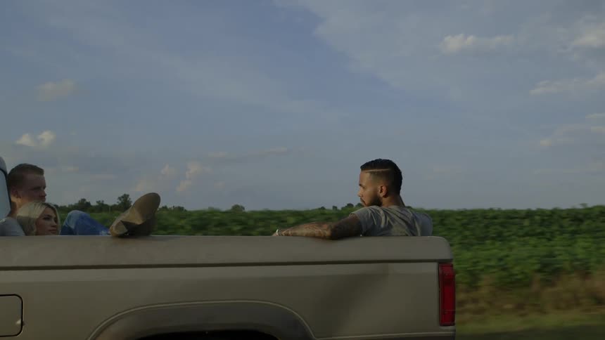 A couple of guys and a girl are sitting in the back of a pickup truck as it goes down the highway