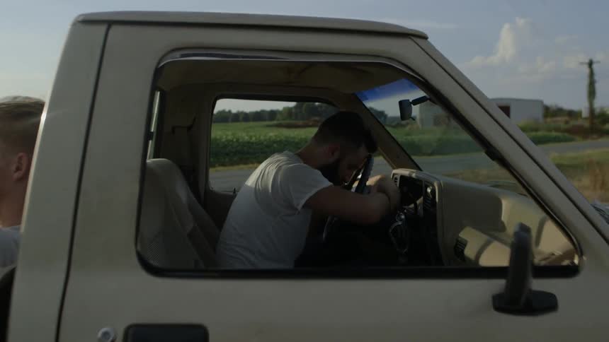 A man sits hunched over a truck steering wheel