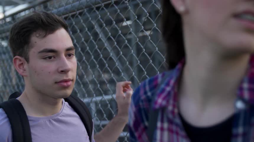 A boy and girl loitering near a fence turn and take off