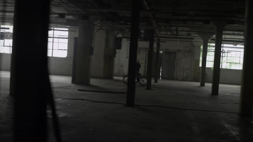 A young man is riding his bicycle in an abandoned building during the day