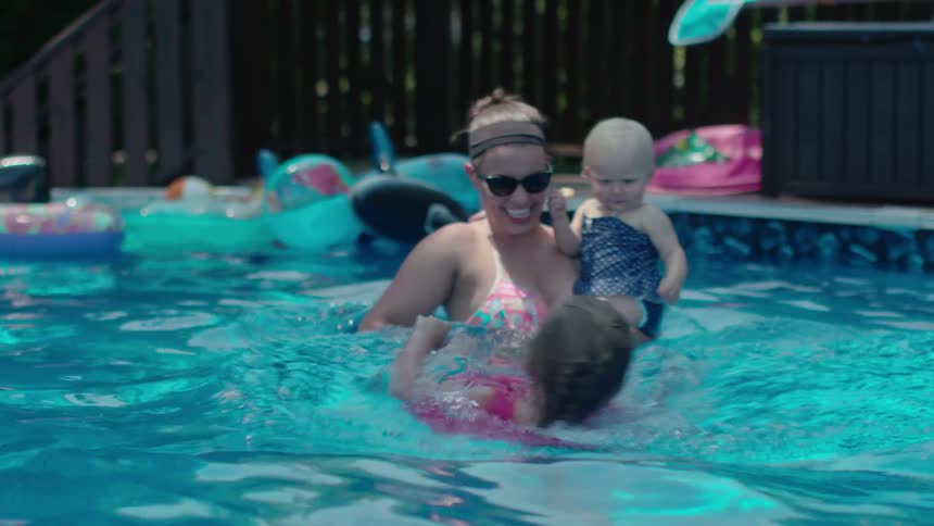 A woman holds a baby while pulling her daughter in the pool