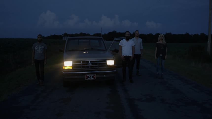 People standing outside of a truck in the country at night