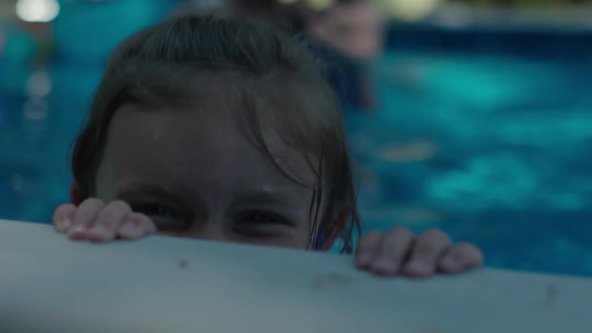 A young girl smiles big as she bobs on the edge of a swimming pool
