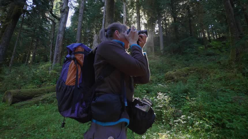 Woman wearing a backpack takes pictures in the woods