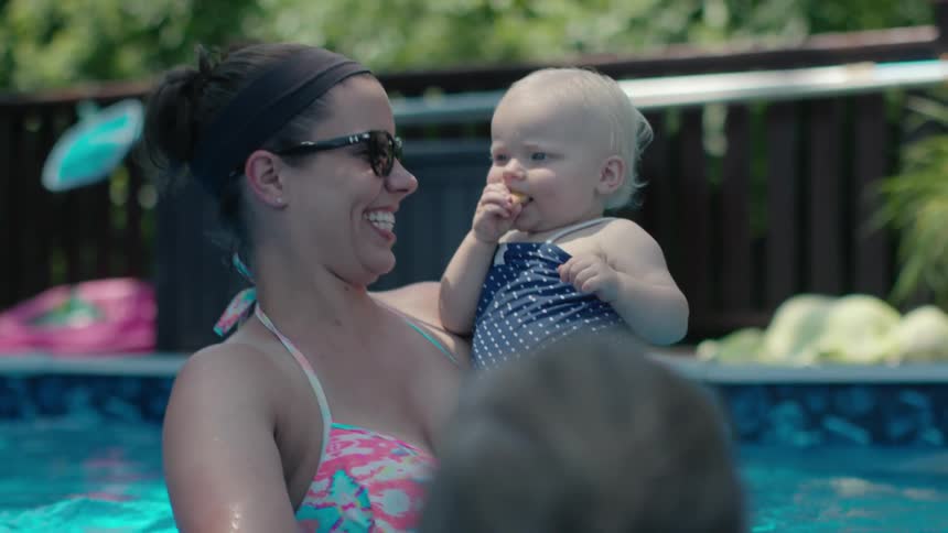 A woman is holding a baby and laughing in the pool