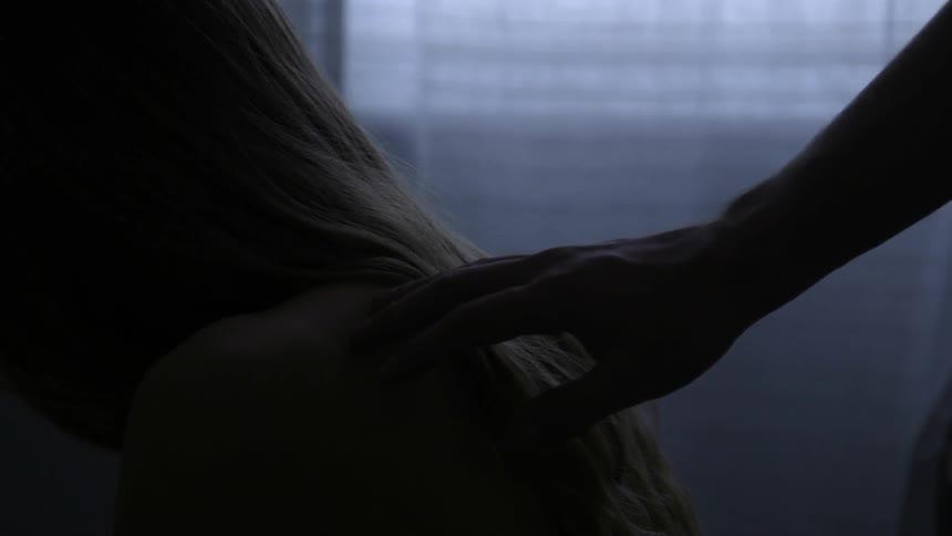 A man reaches out to touch a woman who is sitting still beside a window
