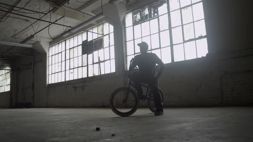 A man is sitting on his bike in an empty warehouse