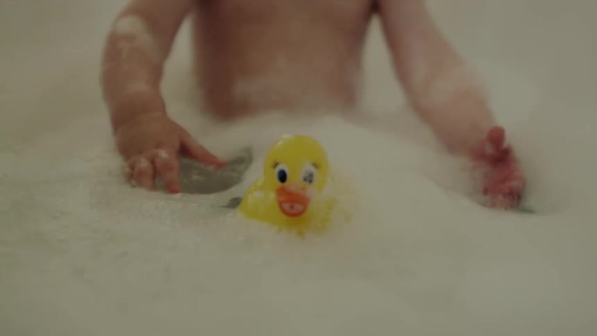 Baby is playing with rubber ducky in the bathtub