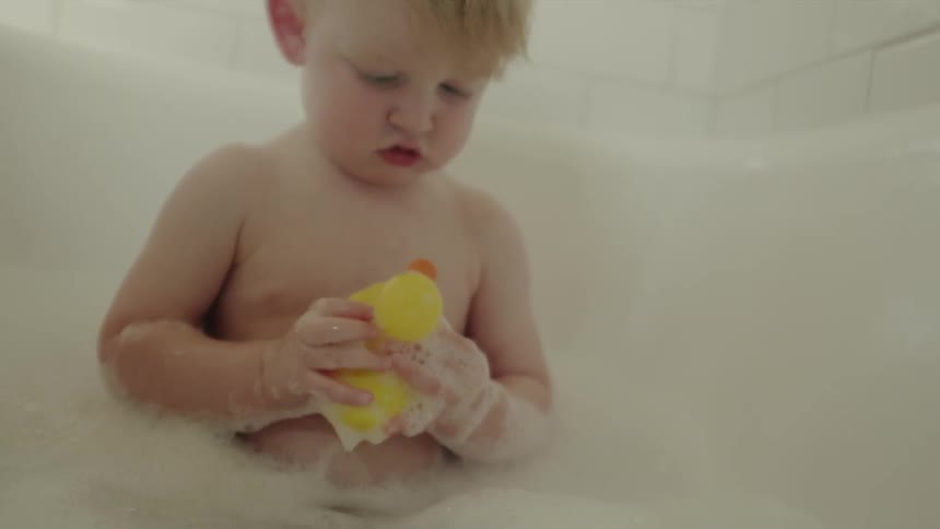 A baby is taking a bubble bath with a rubber ducky