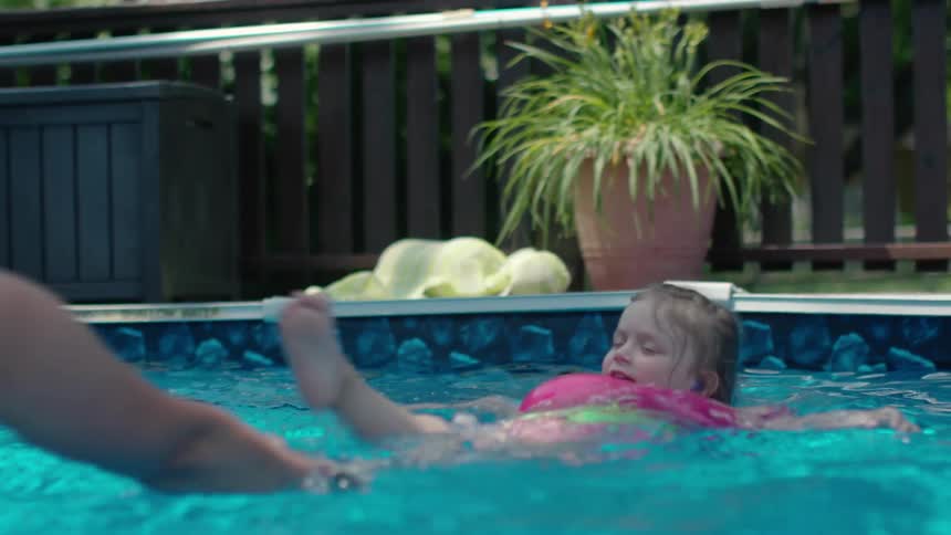 A woman drags a child around on a floatie in the pool