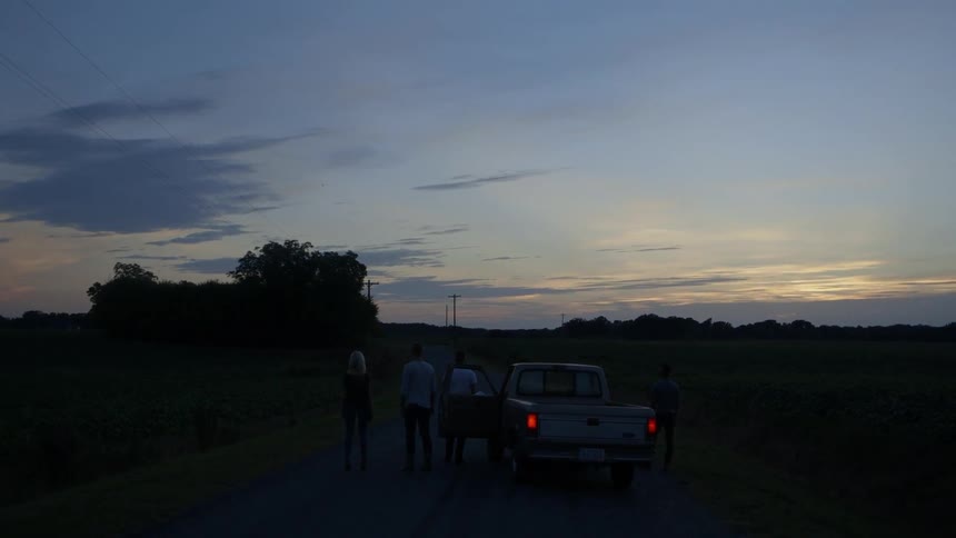 People watch a sunset while standing next to a parked pickup truck