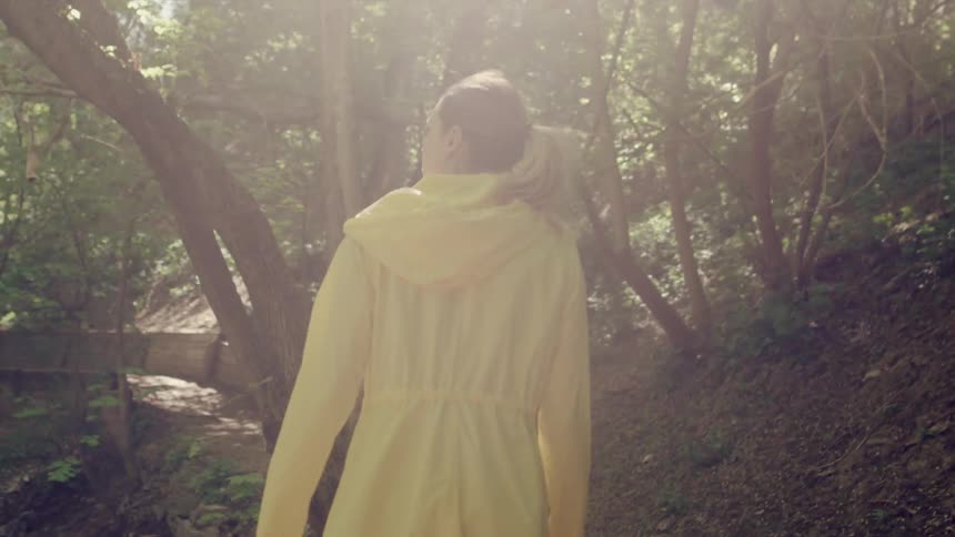 A woman in a yellow coat is walking through the woods