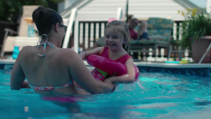 A woman is playing with a little girl in a swimming pool during the day