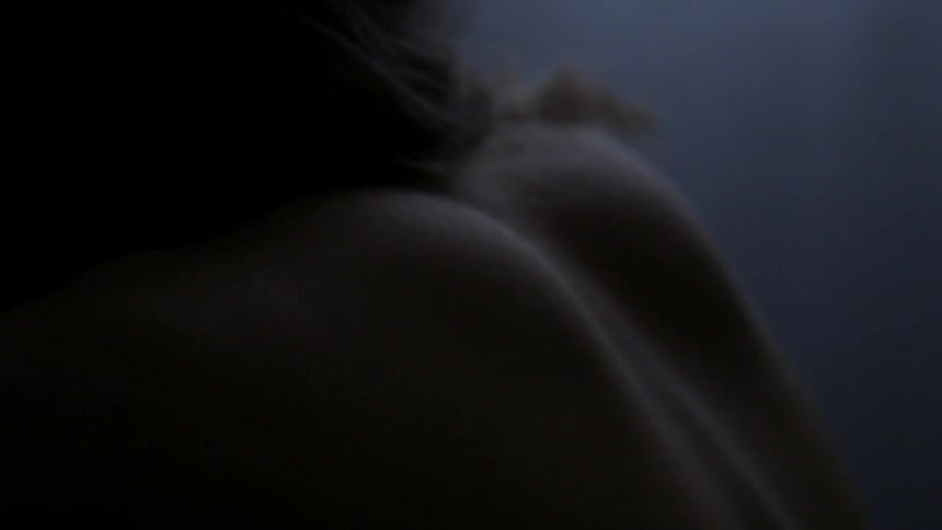 A mans back is shown up close in a dark room